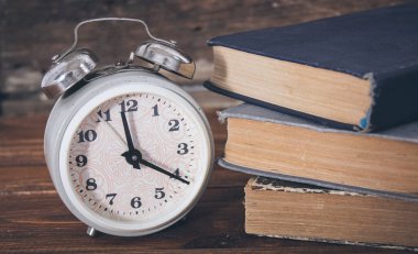 Tahta masadaki çalar saat ve kitaplar.