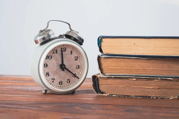Tahta masadaki çalar saat ve kitaplar.