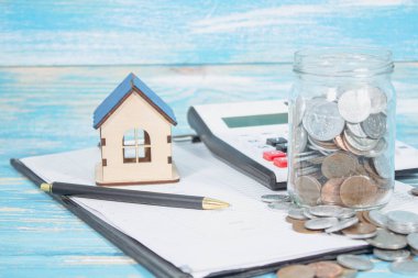 on the table there are papers, a calculator, a house and a bank with coins