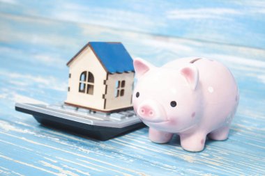 house on a calculator and next to a piggy bank.