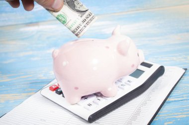 piggy bank on a calculator and papers. puts a dollar bill in a piggy bank.