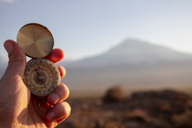 Gün batımında bir dağın arka planında bir pusula tutuyor.