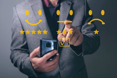 İş adamının eli, işaretli kutunun üzerinde gülen yüz ifadesi ile koyu arkaplandaki sanal dokunmatik ekranda bir işaretle bastırıyor. Müşteri hizmetleri değerlendirmesi, müşteri memnuniyeti devam ediyor