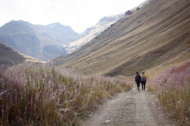 Erkekler dağlarda yürür toprak bir yol boyunca