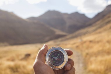 Bir dağ yolunun arka planında bir pusula tutar