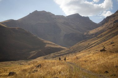 Erkekler dağlarda yürür toprak bir yol boyunca