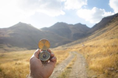 Bir dağ yolunun arka planında bir pusula tutar