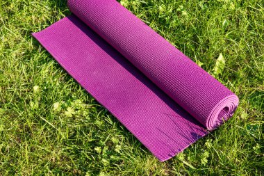 Yeşil çimlerin üzerinde yuvarlanmış Yoga minderi ve güneş ışığı, tam üstte. Açık hava spor konsepti