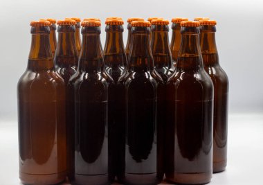 Etiketsiz, beyaz arkaplanlı ev yapımı biralar. Turuncu kapaklı bira şişelerinin yakın plan fotoğrafı. Turuncu kapaklı izole bira şişeleri.. 