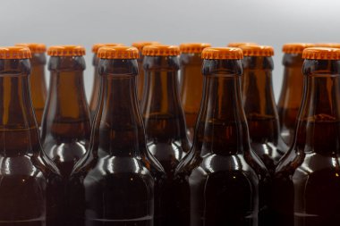 Etiketsiz, beyaz arkaplanlı ev yapımı biralar. Turuncu kapaklı bira şişelerinin yakın plan fotoğrafı. Turuncu kapaklı izole bira şişeleri.. 