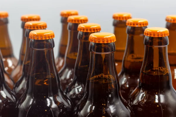 Etiketsiz, beyaz arkaplanlı ev yapımı biralar. Turuncu kapaklı bira şişelerinin yakın plan fotoğrafı. Turuncu kapaklı izole bira şişeleri.. 