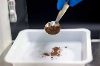 Bilim adamı örneği tartıyor. Dijital analitik denge. Bilim adamının ellerini mavi eldivenlerle kapat. Metal spatulada kahverengi toz örneği var. Laboratuvar kavramı. 