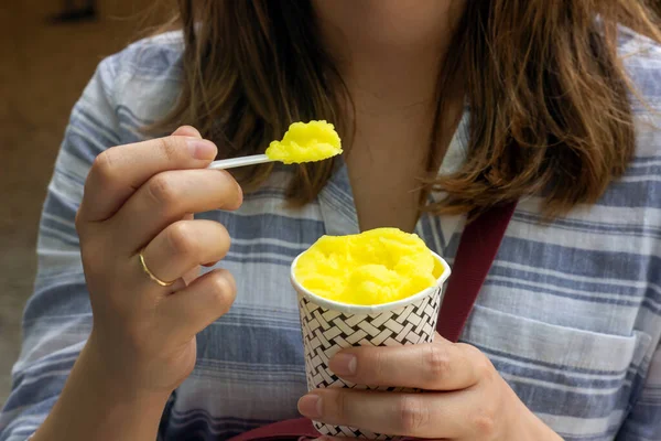 The woman eating yellow ice cream. Lemon ice cream. The woman holding lemon ice cream. Ice cream in the cup.