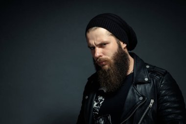 Deri ceketli, şapkalı ve kameraya bakan yakışıklı sakallı adamın portresi..