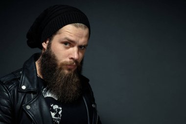Deri ceketli, şapkalı ve kameraya bakan yakışıklı sakallı adamın portresi..