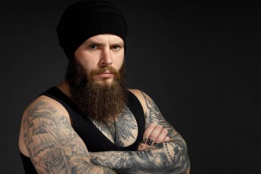 Siyah tişörtlü ve şapkalı, kameraya bakan yakışıklı sakallı bir adamın portresi..