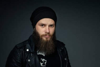 Deri ceketli, şapkalı ve kameraya bakan yakışıklı sakallı adamın portresi..