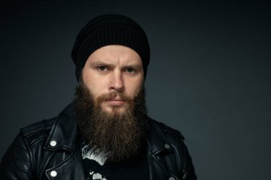 Deri ceketli, şapkalı ve kameraya bakan yakışıklı sakallı adamın portresi..