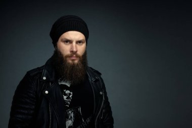 Deri ceketli, şapkalı ve kameraya bakan yakışıklı sakallı adamın portresi..