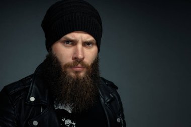 Deri ceketli, şapkalı ve kameraya bakan yakışıklı sakallı adamın portresi..