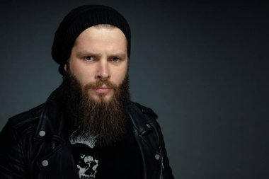 Deri ceketli, şapkalı ve kameraya bakan yakışıklı sakallı adamın portresi..