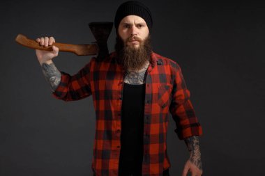 Uzun saçlı, elinde baltası olan yakışıklı bir adam karanlık bir stüdyo geçmişinde..