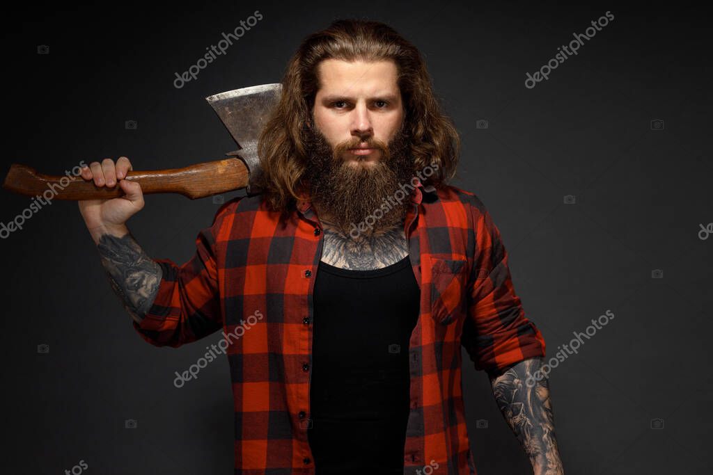 Handsome man with long hair with an ax in his hands on a dark studio background.