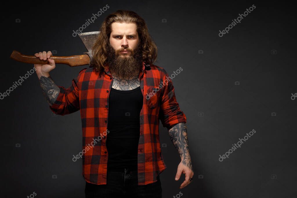 Handsome man with long hair with an ax in his hands on a dark studio background.
