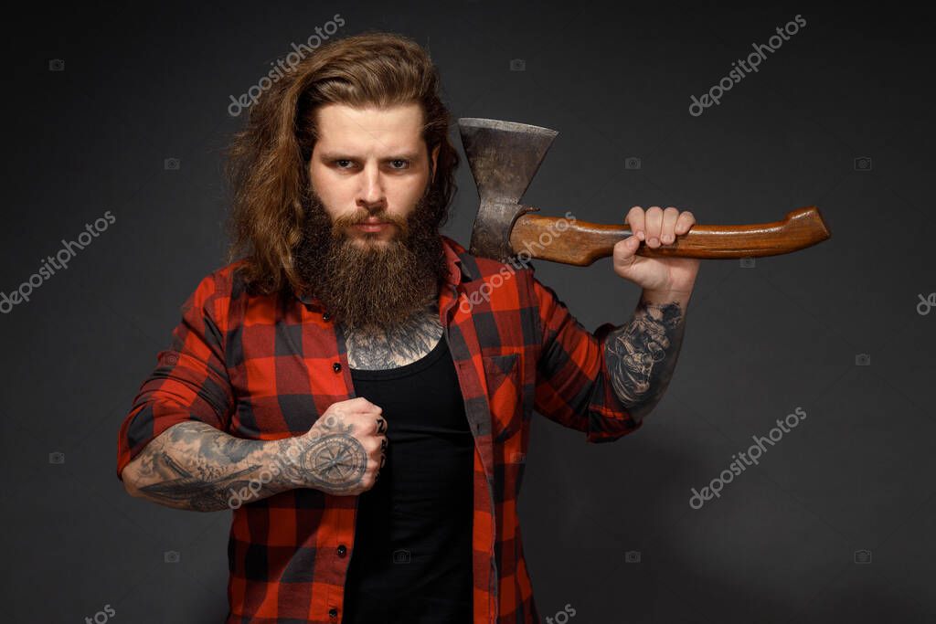 Handsome man with long hair with an ax in his hands on a dark studio background.