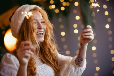 Noel Baba şapkalı güzel kızıl saçlı kız ellerinde maytaplarla kameraya gülümsüyor..