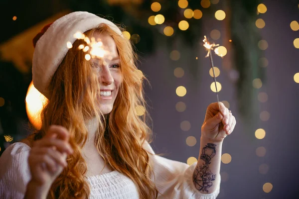 Noel Baba şapkalı güzel kızıl saçlı kız ellerinde maytaplarla kameraya gülümsüyor..