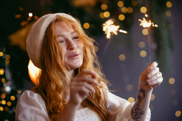 Noel Baba şapkalı güzel kızıl saçlı kız ellerinde maytaplarla kameraya gülümsüyor..