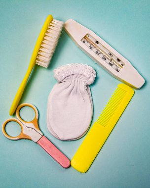 bebek tarakları, termometre, bebek makasları ve mavi arka planda popolar.