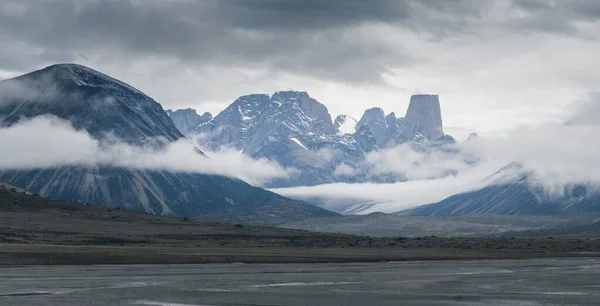 Ikonisk granittfjell av Mt.Åsgard-tårn over Turners isbre på en svært overskyet og tåkete dag i den fjerne arktiske dalen Akshayuk-passet på Baffinøya i Canada. Landskap i avsidesliggende villmark langt nord. – stockfoto