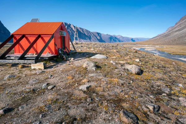 Owl River emergency shelter in remote arctic wilderness with a backpack in front of it . Sunny day in Akshayuk Pass valley, Auyuittuq National Park, Baffin Island, Nunavut, Canada.