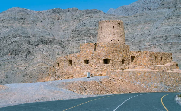 Murallas de piedra de pequeño fuerte árabe medieval bajo altos acantilados de montaña. Fortaleza en Bukha, península de Musandam, Omán. Día caluroso y nebuloso en el desierto árabe. — Foto de Stock