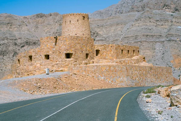 Murallas de piedra de pequeño fuerte árabe medieval bajo altos acantilados de montaña. Fortaleza en Bukha, península de Musandam, Omán. Día caluroso y nebuloso en el desierto árabe. — Foto de Stock