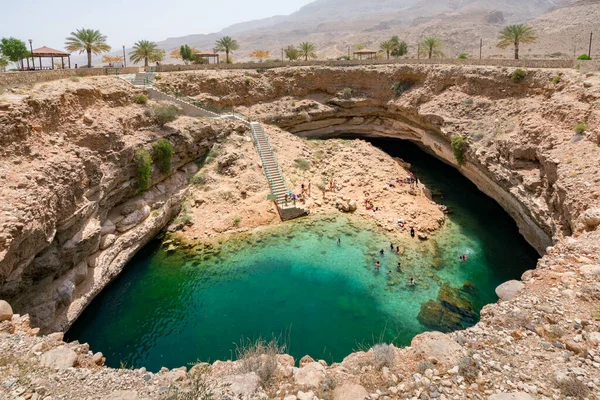 Bimmah, Omán - 04.05.2018: Gente nadando y colgando alrededor de aguas turquesas de la piscina del sumidero de Bimmah, o Hawiyyat Najm, laguna de agua de mar en el desierto de Omania. — Foto de Stock