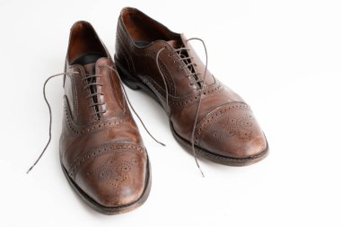 Studio shot of old, weary and little scratched cap toe lace op oxford shoes in burnished brown color, on white background. Old shoes, with laces out, before cleaning and polishing.
