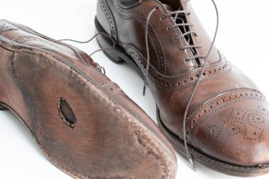 Studio shot of old, weary and little scratched cap toe lace op oxford shoes in burnished brown color, on white background. Hole in the sole of the right shoe. Old shoes that need repair.