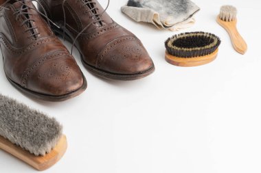 Studio shot of old, weary and little scratched cap toe lace op oxford shoes in burnished brown color, on white background. Three brushes of different sized and dirty cleaning cloth.