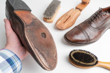 Studio shot of old, weary, little scratched cap toe lace op oxford leather shoes in burnished brown color on white background, in left male hand. Hole in the shoe sole. Old shoes that need a repair.