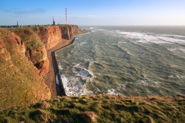 Heligoland adasının engebeli kırmızı uçurumları ve arkada deniz feneri. Kuzey Denizi, Almanya 'da Helgoland' da güneşli bir kış günü.
