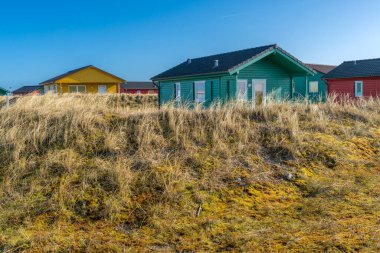 Dune, Almanya - 02.27.2022: Kışın güneşli bir günde kumlu kum tepelerindeki renkli ahşap kulübeler. Plajdaki tatil evleri. Deniz kenarında konaklama.