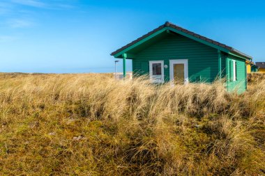 Dune, Almanya - 02.27.2022: Kışın güneşli bir günde kumlu kum tepelerindeki renkli ahşap kulübeler. Plajdaki tatil evleri. Deniz kenarında konaklama.