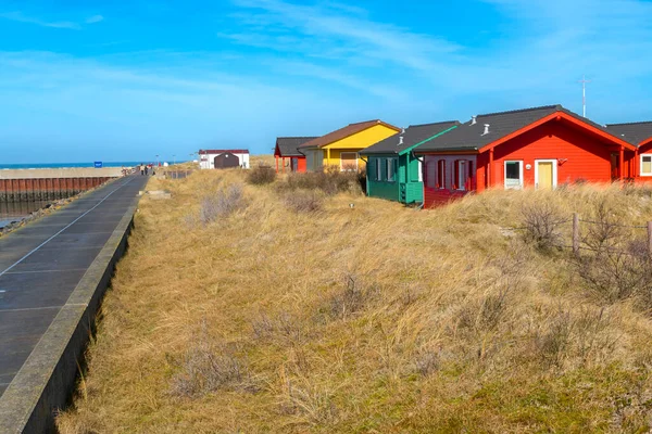 Dune, Alemania - 02.27.2022: Cabañas de madera coloridas en dunas de arena con hierba amarilla en un hermoso día soleado de invierno. Casas de vacaciones en la playa. Alojamiento junto al mar. — Foto de Stock