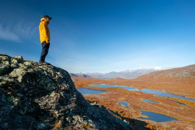 İsveç 'in sonbahar günü, Stora Sjofallet Ulusal Parkı' nın uçsuz bucaksız arktik manzarasına bakan erkek yürüyüşçü. Laponya 'nın dağları ve vadileri. Ahkka massif. Lulep Gierkav 'ın tepesinden görüntüle.