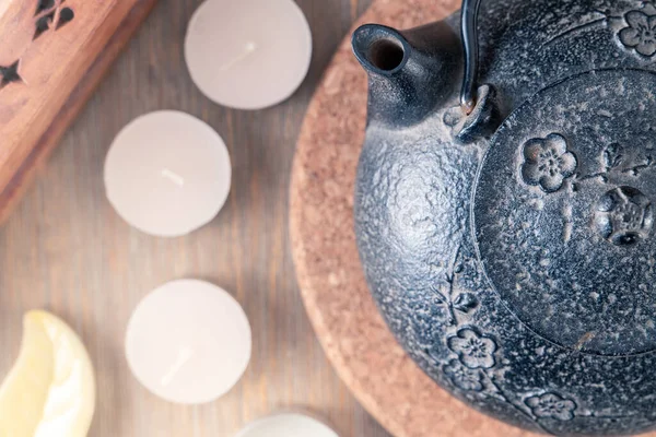 Teiera giapponese in metallo nero su un tavolo di legno con candele da tè e scatola di legno di bastoncini profumati. Natura morta in stile zen in colori caldi e pacifici. Tè caldo per il momento di meditazione. — Foto Stock