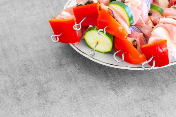 Çiğ hindi şiş kebap, metal şiş kebap, bir sürü renkli sebzelerle birlikte, beyaz tabakta, hazırlanmaya hazır. Açık gri dizayn masası yüzeyi. Lezzetli, hafif, harika görünen yemekler..