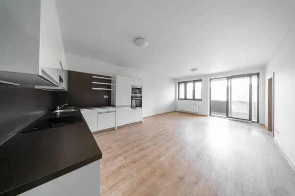 Celadna, Czechia - 05.07.2022: Empty room with wooden floor and white and black modern design kitchen. White walls and ceiling. — стоковое фото